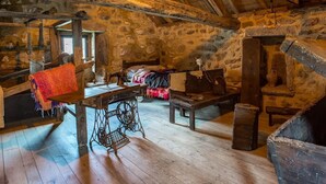 Una habitación rústica con paredes de piedra, vigas de madera, una mesa de madera, un banco y una máquina de coser.