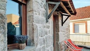 Un edificio de piedra con una ventana, una puerta y un balconcito con una silla roja.