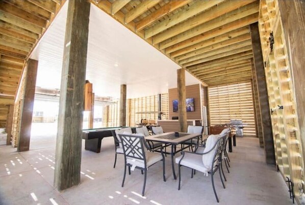 Espaço de lazer coberto com mesa de bilhar, assentos e estrutura de teto em madeira.