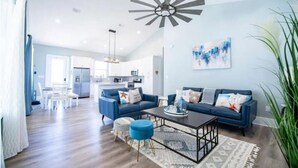A spacious living room with a blue sofa set, a coffee table, and a modern ceiling fan.
