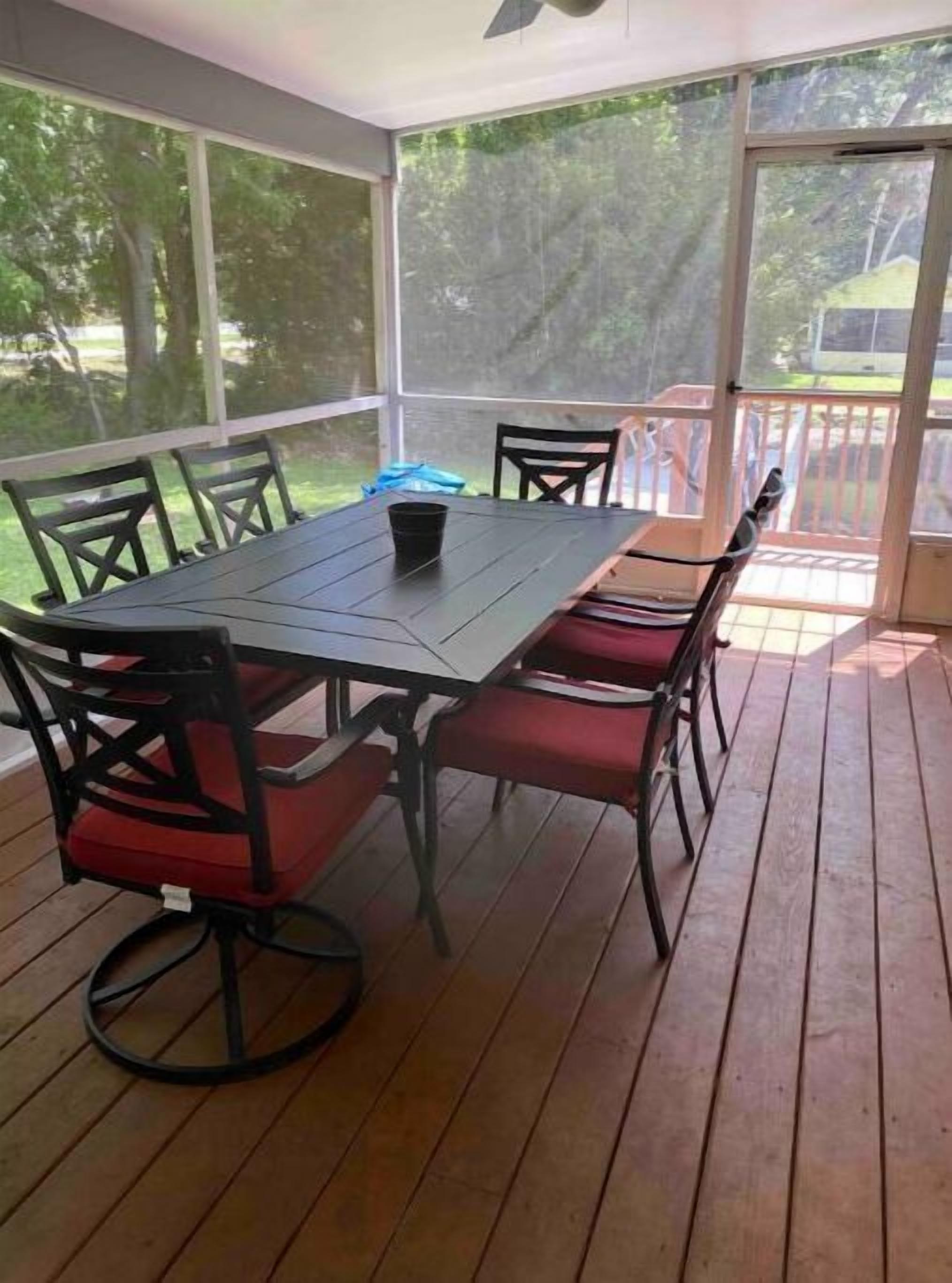 A covered patio with a table and chairs, large windows, and a view of the outdoors.