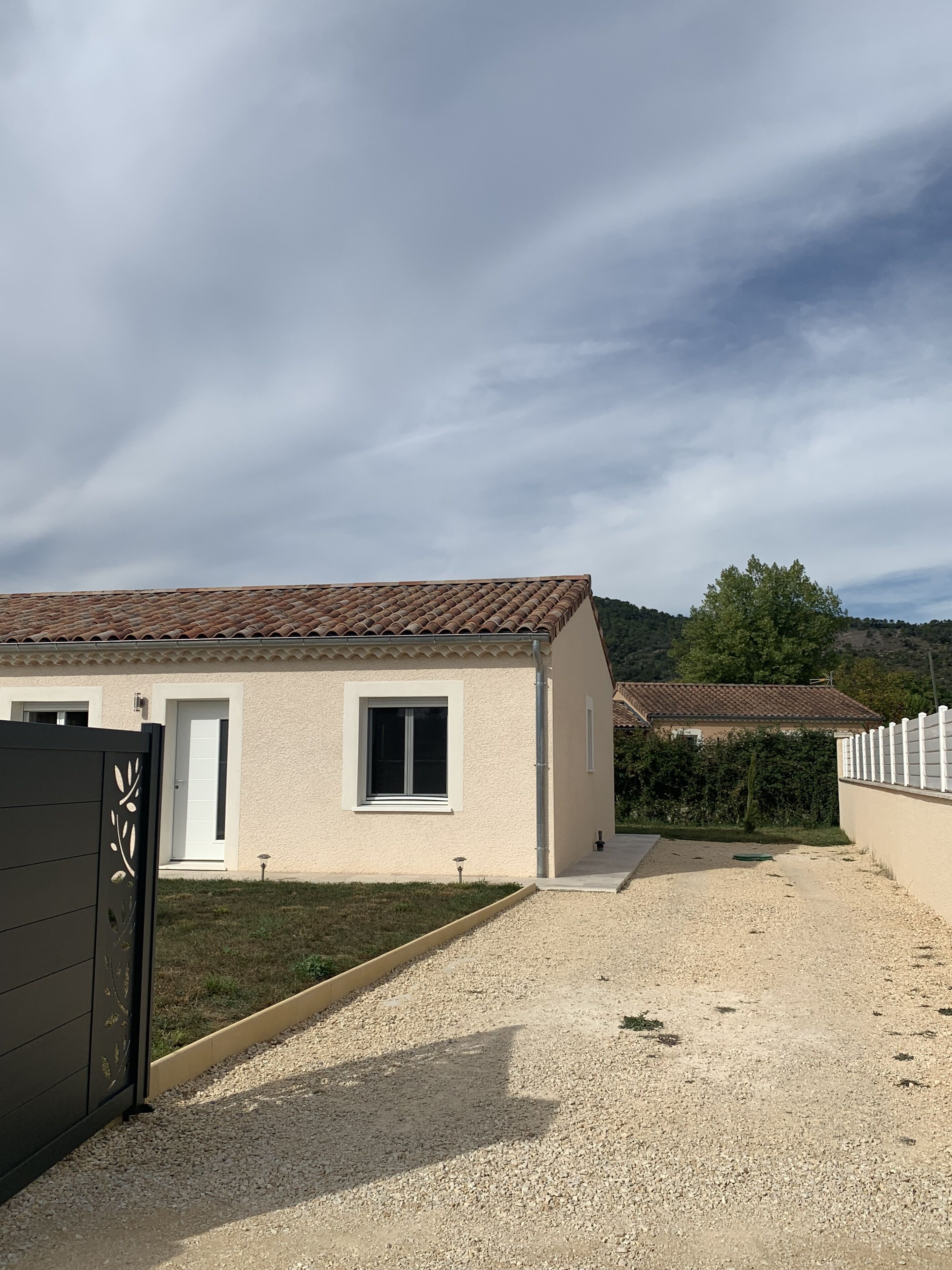 Uma casa térrea com telhado de cerâmica, entrada por um caminho de brita e cerca branca.