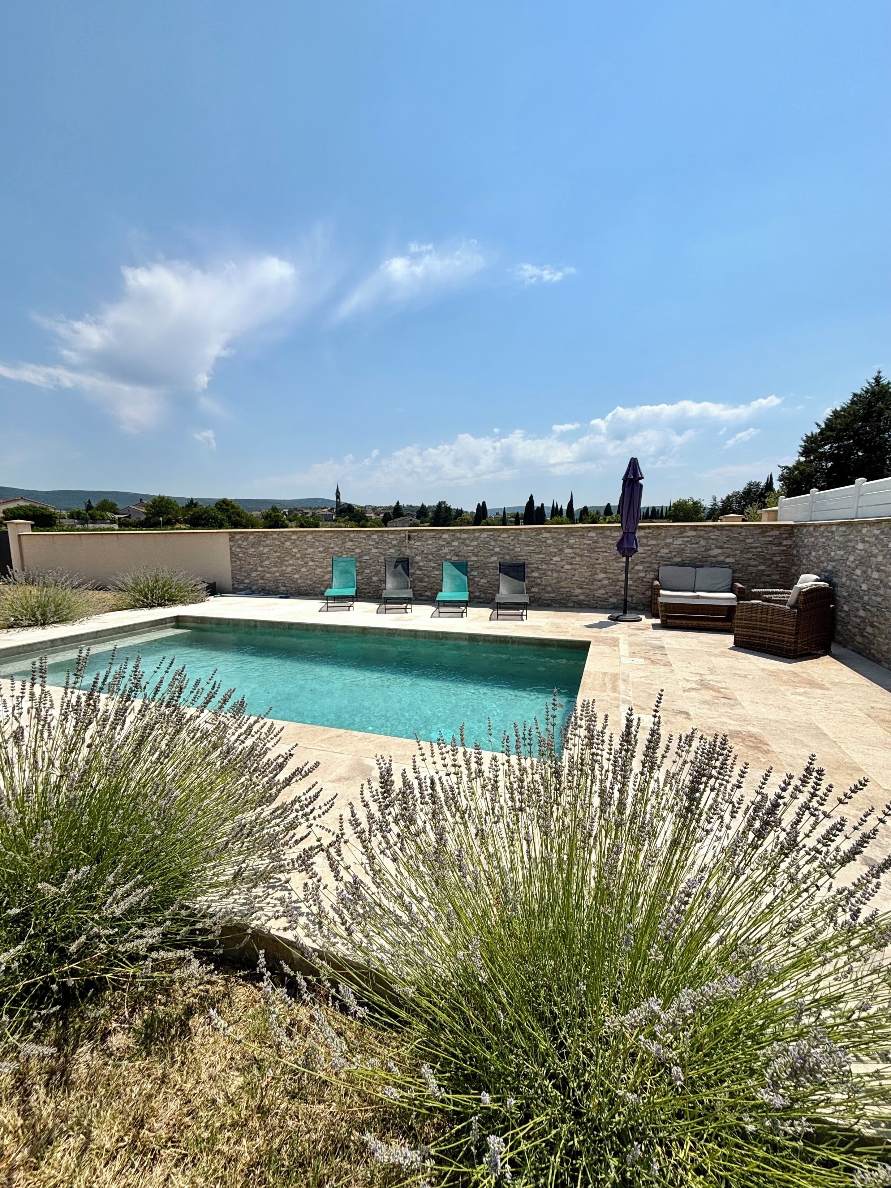 Une piscine avec des chaises longues et un mur en pierre.