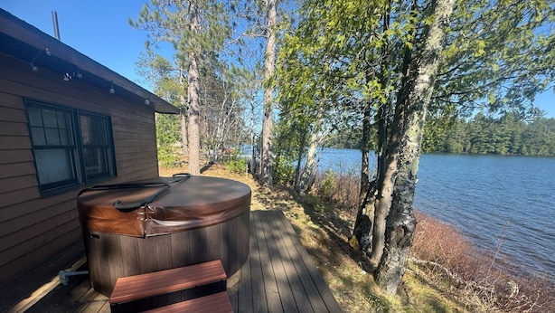 Een houten terras met een jacuzzi en een trap naar een hutje aan het meer.