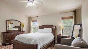 Un dormitorio con cama de madera, una mesita de noche, una silla, un espejo y una ventana con cortinas.