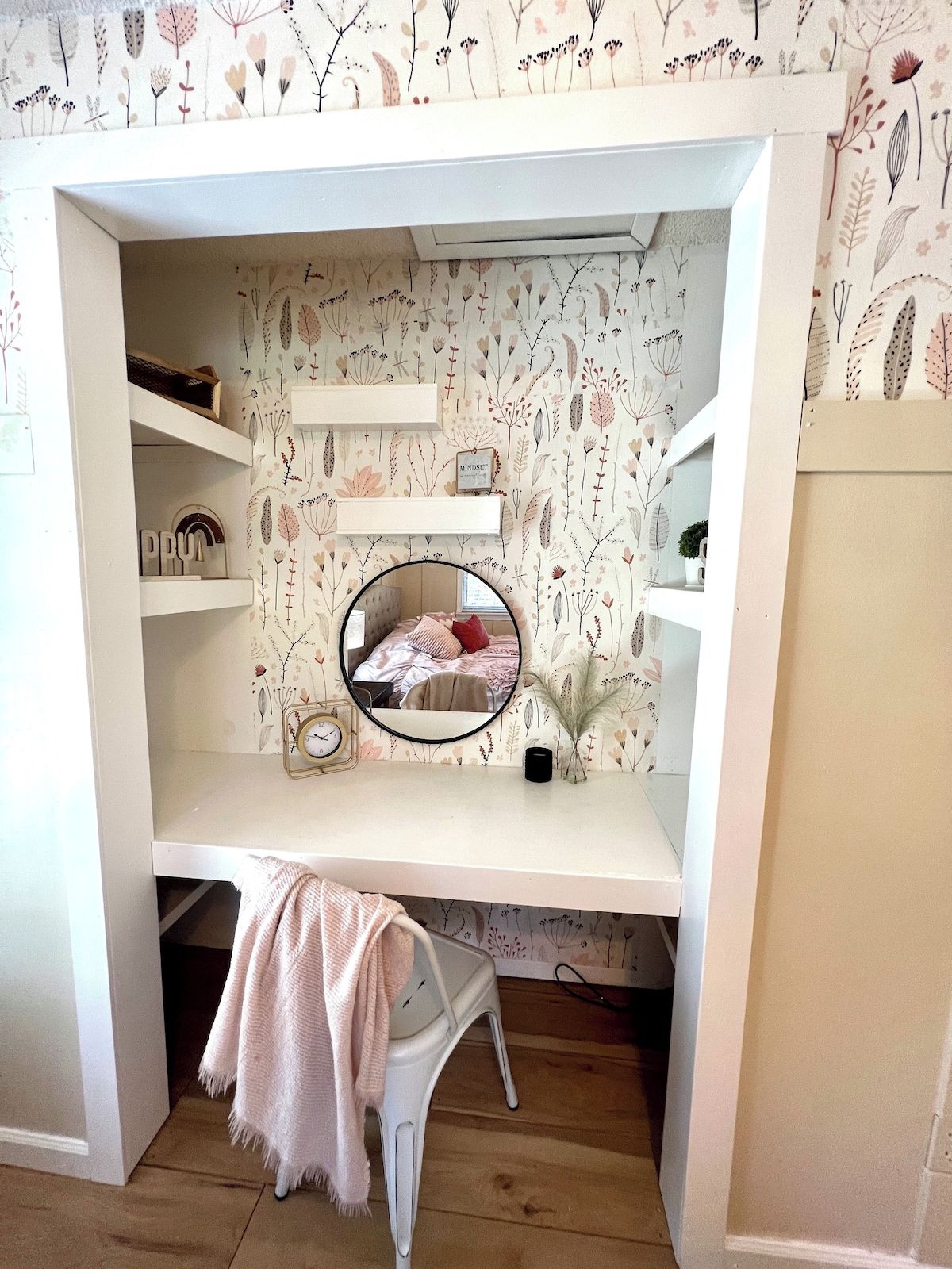 A cozy bedroom with a built-in desk, a mirror, and a shelf unit.