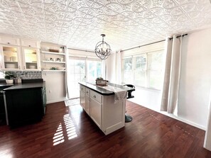 A kitchen with a central island, white cabinetry, and a decorative ceiling. - Sunshine Cottage | Near Whitewater Park | Sleeps 10 (Norfolk)