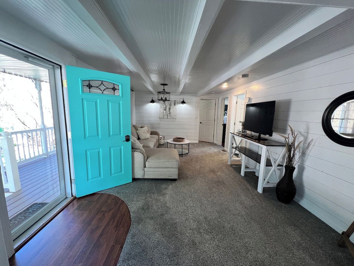 A living room with a teal door, a sofa, a coffee table, a TV, and a round window.