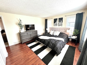A bedroom with a bed, dresser, TV, and a window with curtains. - Sunshine Cottage | Near Whitewater Park | Sleeps 10 (Norfolk)