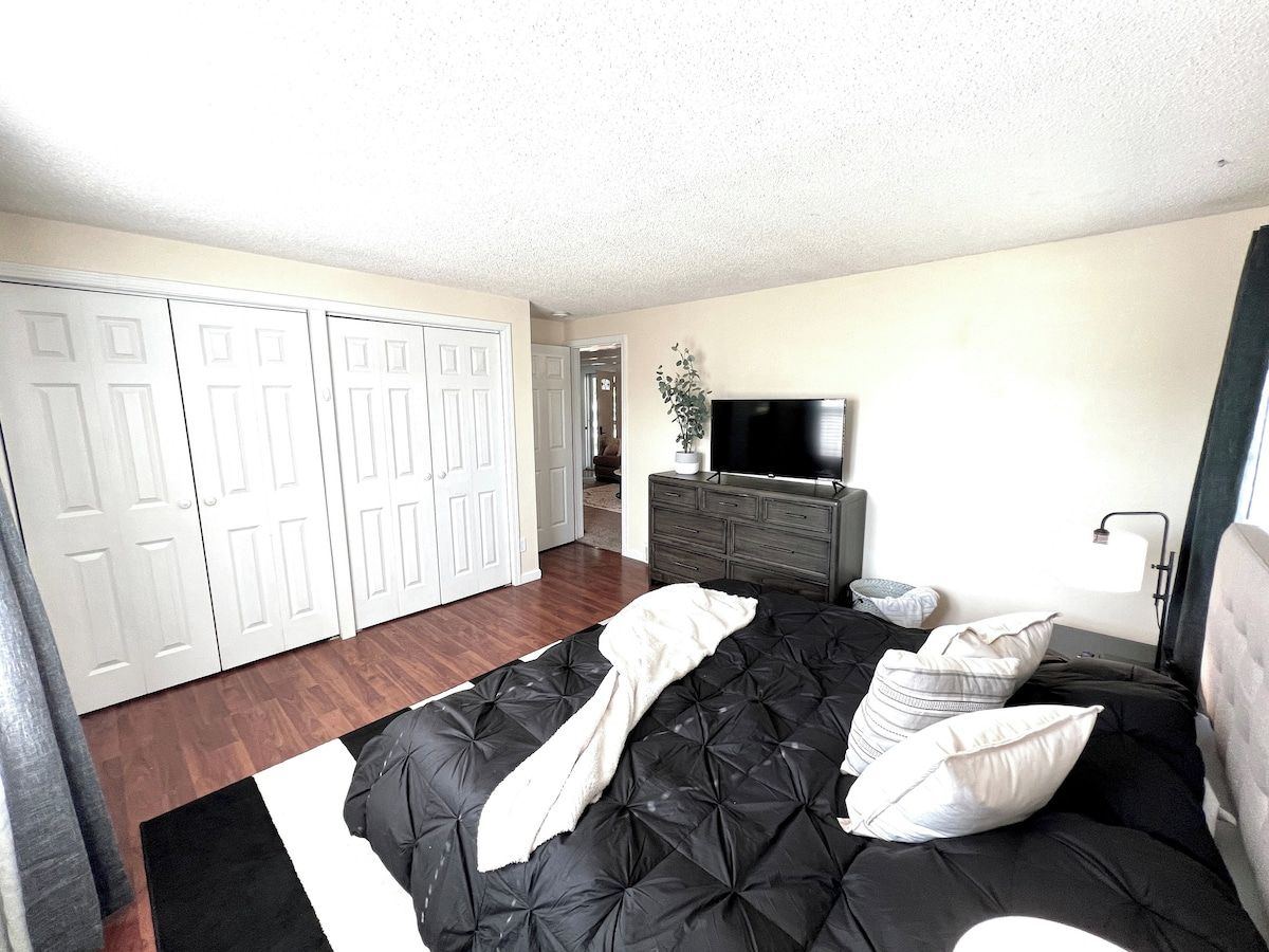A room with a black sofa, white pillows, a television on a dresser, and a door leading to another room.