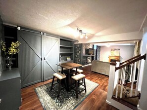 A dining area with a wooden table and four chairs, a sliding door closet, a kitchen with a microwave, and a staircase. - Sunshine Cottage | Near Whitewater Park | Sleeps 10 (Norfolk)
