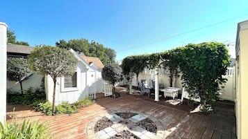 A wooden deck with a circular fire pit, surrounded by potted plants and a white fence.