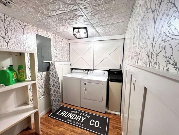 A laundry room with a washing machine, dryer, and shelves with cleaning supplies. - Sunshine Cottage In Norfolk (Norfolk)