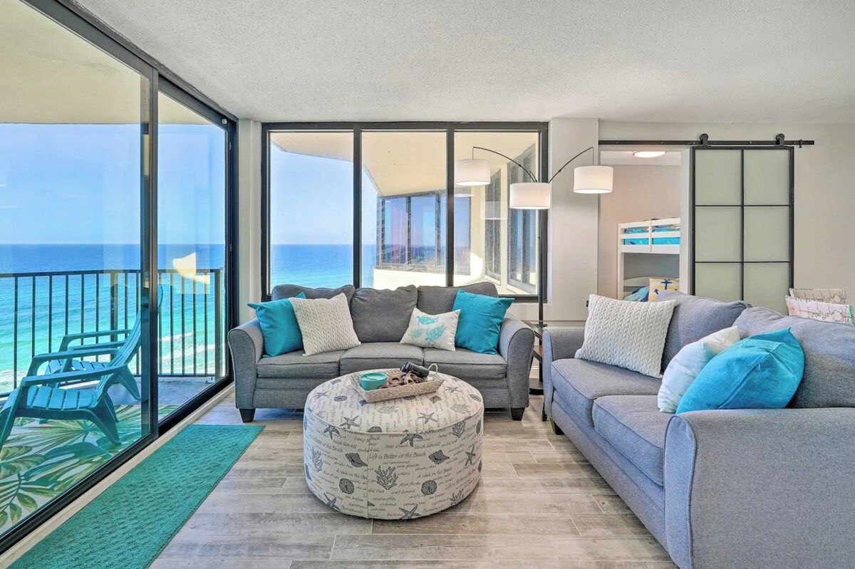 A modern living room with a grey sofa, ottoman, and a view of the ocean.