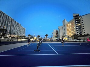 Un court de tennis en plein air, avec un filet au centre, entouré de grands immeubles.