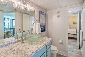 Une salle de bain avec un lavabo en verre, deux robinets, un miroir et des toilettes.