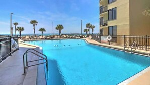 A swimming pool with lounge chairs and palm trees, surrounded by a building with balconies.