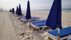 A beach with rows of blue beach umbrellas and white lounge chairs.
