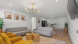 A modern living room with a grey sofa, yellow armchairs, and a dining area with a table and chairs. - Long Bay Duplex Lower Unit by the Beach (Surfside Beach)