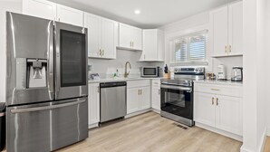A modern kitchen with stainless steel appliances, white cabinetry, and a wooden floor. - Long Bay Duplex Lower Unit by the Beach (Surfside Beach)