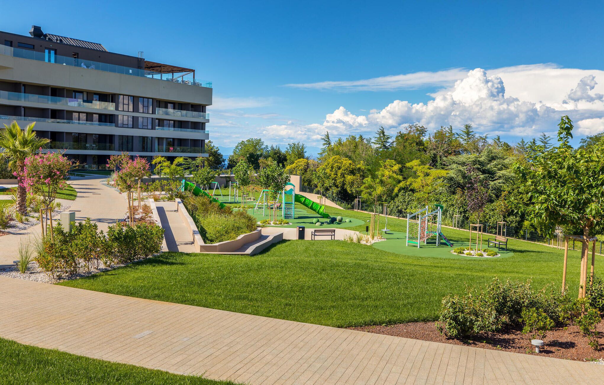 Ein modernes Gebäude mit Dachterrasse und einem gepflegten Park mit Spielgeräten.