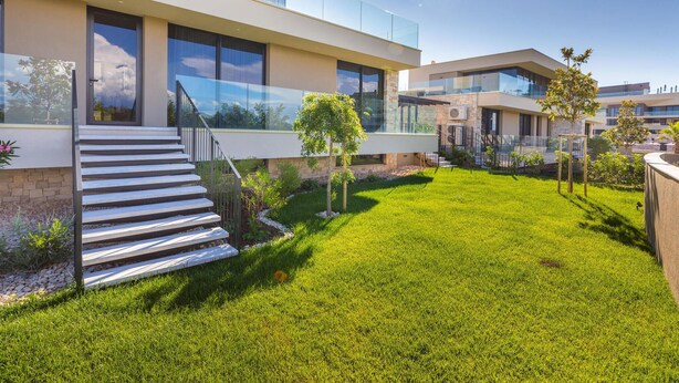 A modern house with a glass balcony, a staircase leading to the entrance, and a well-maintained lawn.