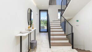A modern staircase with a glass door leading to a balcony, a white console table with a lamp and candle, and a marble floor.