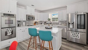A modern kitchen with white cabinets, stainless steel appliances, and a central island with two teal bar stools. - Stylish 5BR 3BA Home w/Pool Perfect for 16ppl (Allen)