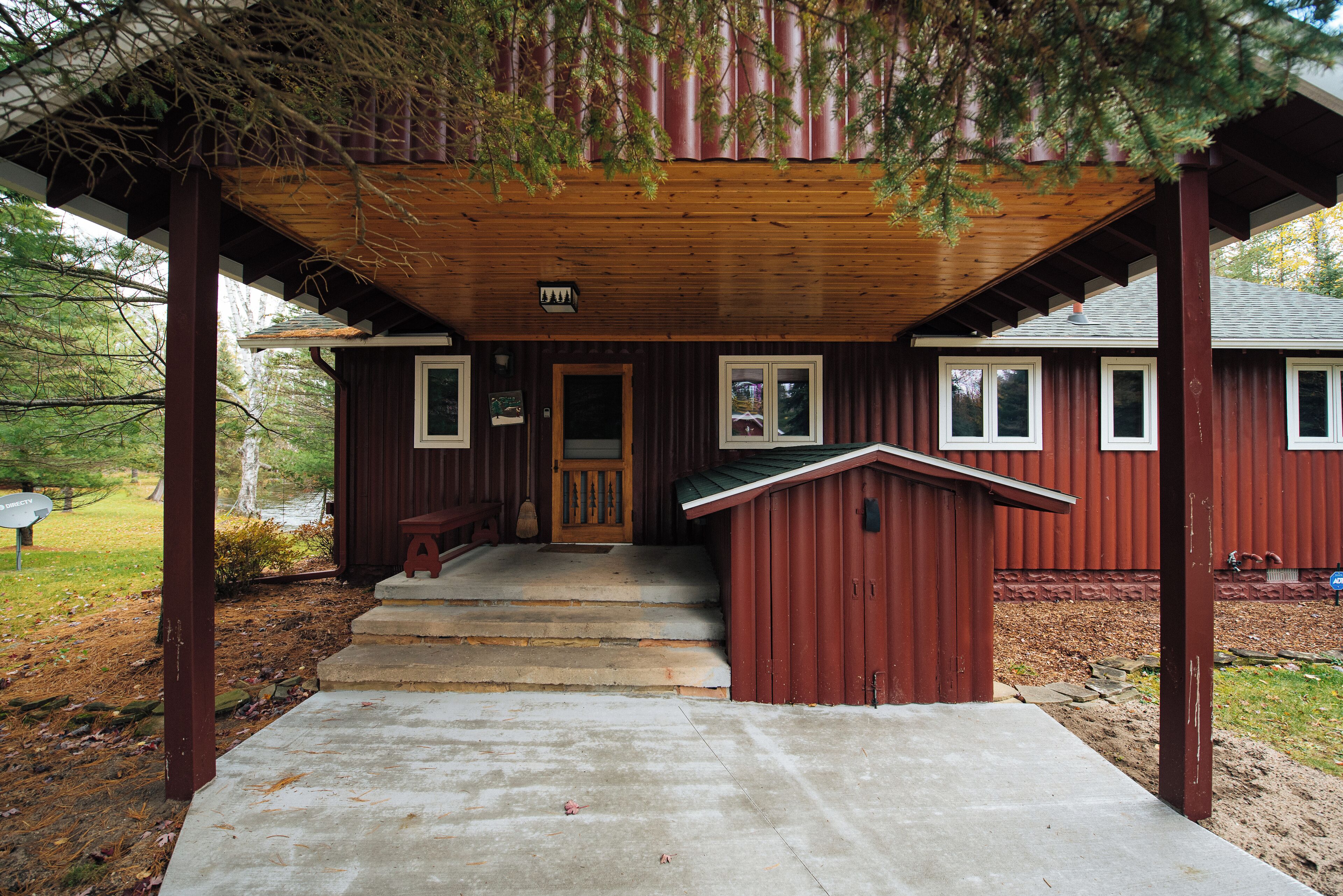 A wooden cabin with a porch, steps leading to the entrance, and a small shed.