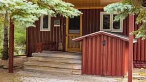 A wooden cabin with a porch, steps, and a door. - Cozy Riverside Getaway Pine Bend Cottage (Grayling)