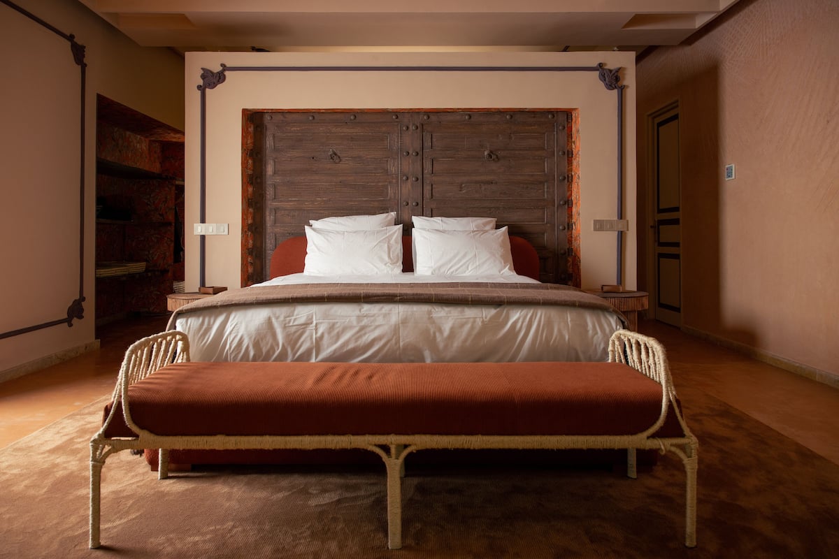 Een slaapkamer met een groot bed, een houten hoofdbord, een bankje en een nachtkastje.