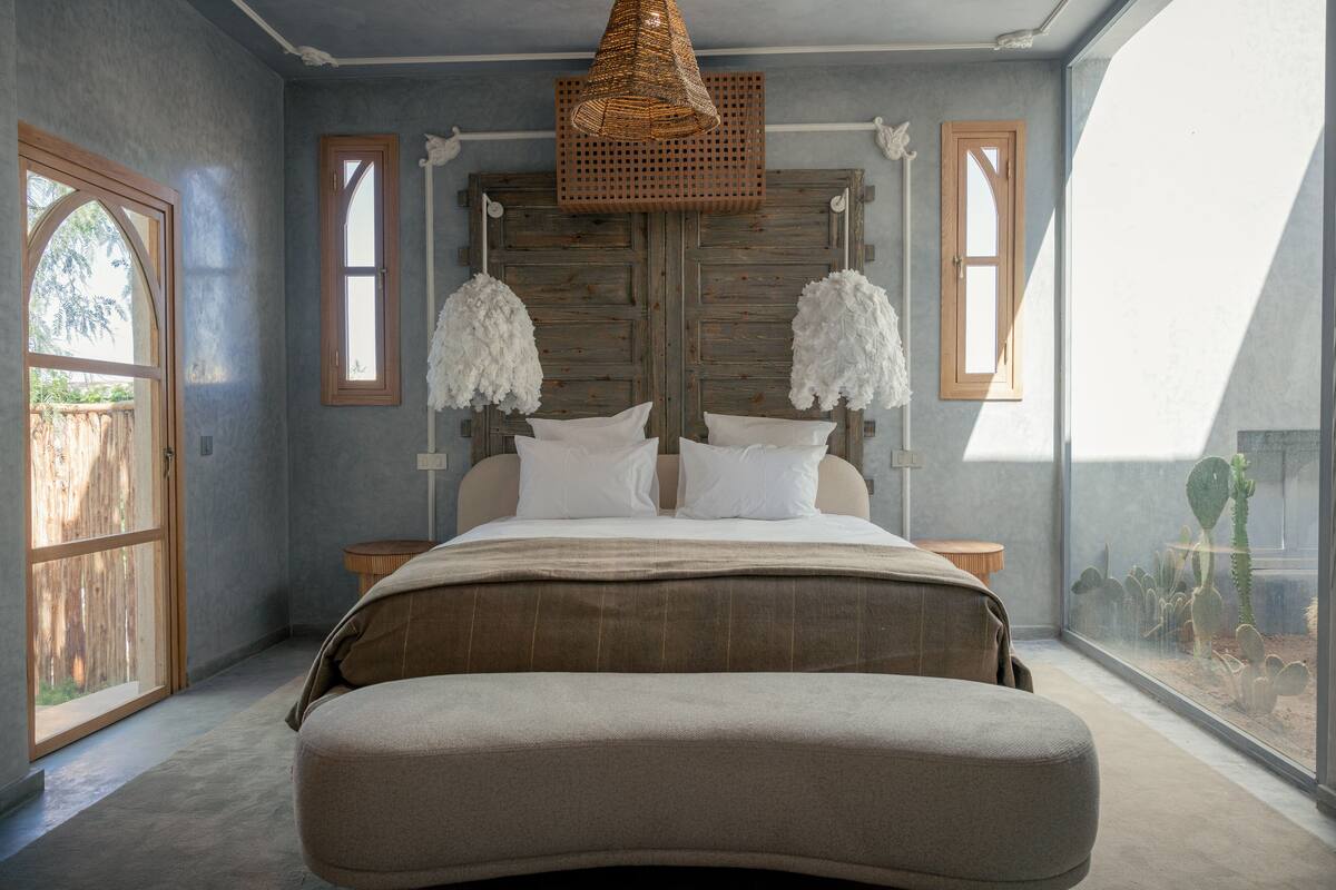 Een slaapkamer met een groot bed, twee nachtkastjes, een hanglamp en een raam met uitzicht op een cactus.