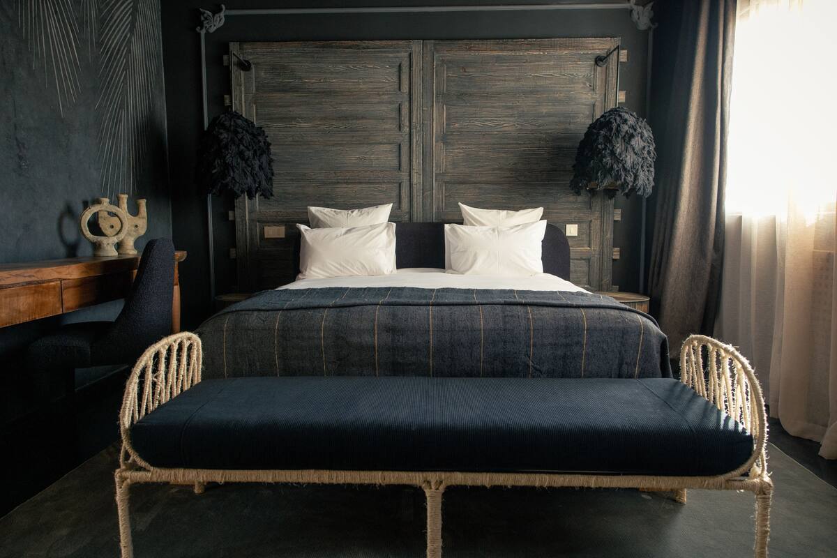 Een slaapkamer met een groot bed, twee bedlampjes, een houten hoofdbord en een bankje aan het voeteneinde.