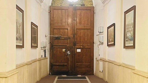 Un pasillo con una puerta grande de madera, paredes blancas y suelo de baldosas.