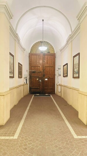 A hallway with a large wooden door, white walls, and a tiled floor. - Anas Prime Place (Rome)