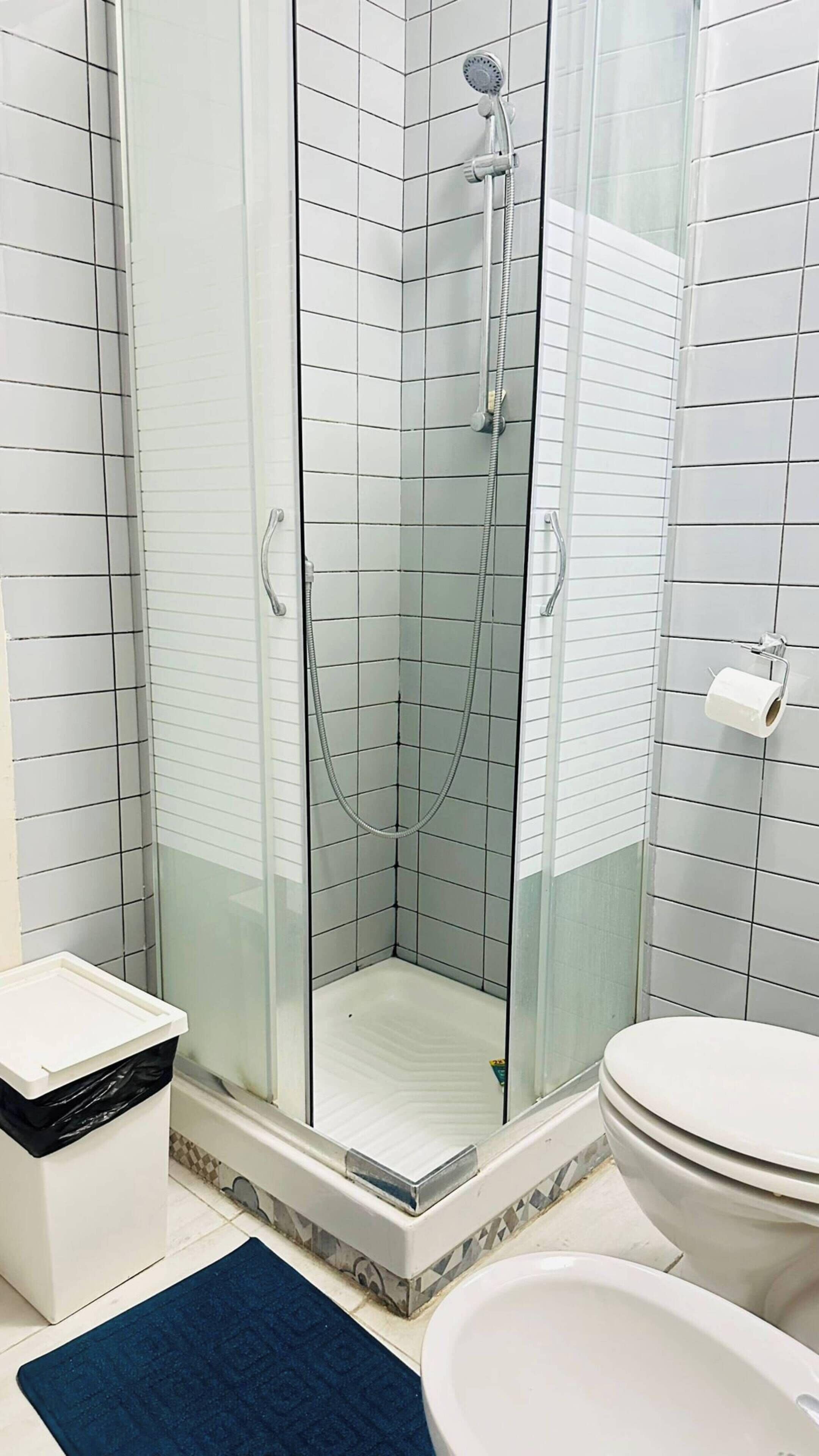 A modern bathroom with a glass-enclosed shower, a white toilet, and a trash bin.