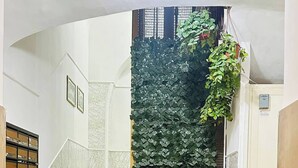 Una escalera con un muro cubierto de hojas verdes, escalones de mármol y una lámpara en el techo.