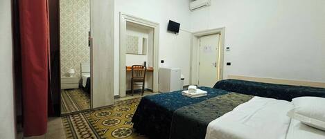 Habitación de hotel con cama, escritorio, silla, refrigerador pequeño y televisión.