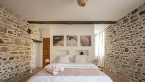 A bedroom with a stone wall, a bed with a white quilt, and three framed pictures on the wall. - Ferme Sarthou, 14 Personnes, Avec Piscine, 5 Étoiles (Lucq-de-Béarn)