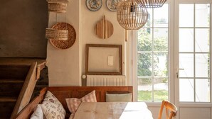 A cozy dining area with a wooden table, wicker hanging lights, and a view through a large window. - Ferme Sarthou, 14 Personnes, Avec Piscine, 5 Étoiles (Lucq-de-Béarn)