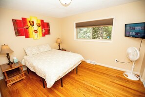 A bedroom with a bed, bedside tables, a lamp, a wall-mounted TV, and a window with blinds. - Walk to Sycamore Mall, 5 Min Drive To City Center, 8 Beds Home, Fenced Yard (Iowa City)
