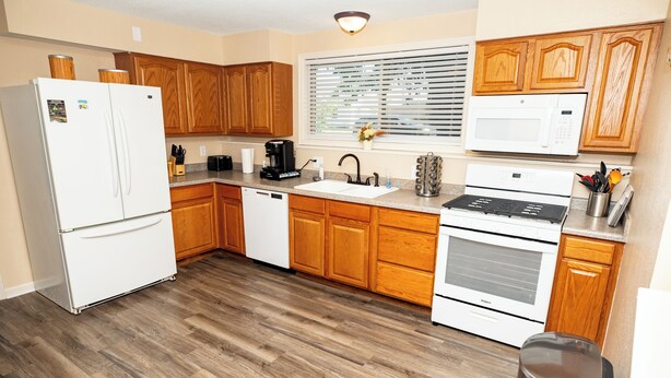 A modern kitchen with wooden cabinets, a stainless steel sink, a white refrigerator, a microwave, and a dishwasher.