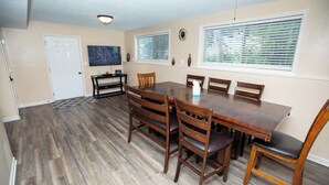 A dining area with a wooden table and chairs, a door, a window with blinds, and a wall-mounted clock.
