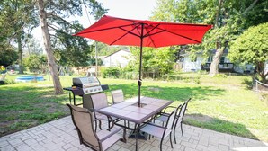 A patio with a table and chairs, a barbecue grill, and a red umbrella.