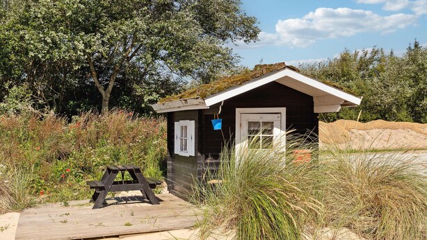 Un petit chalet de plage avec une porte et des fenêtres, une table de pique-nique et une terrasse en bois.