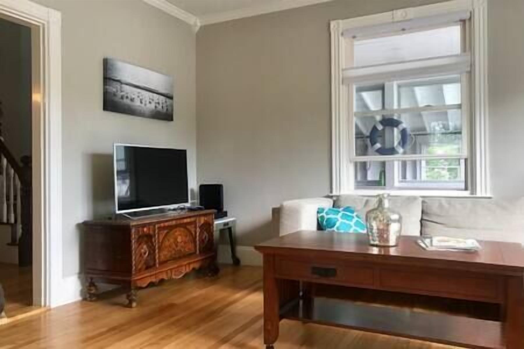 Un soggiorno con una TV a schermo piatto su un mobile in legno, un divano con un cuscino decorato e una finestra vista aperta.