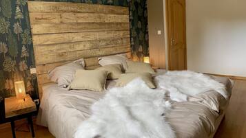 A bedroom with a wooden headboard, a bed with beige bedding and white pillows, a small bedside table with a lamp, and a door to the right.