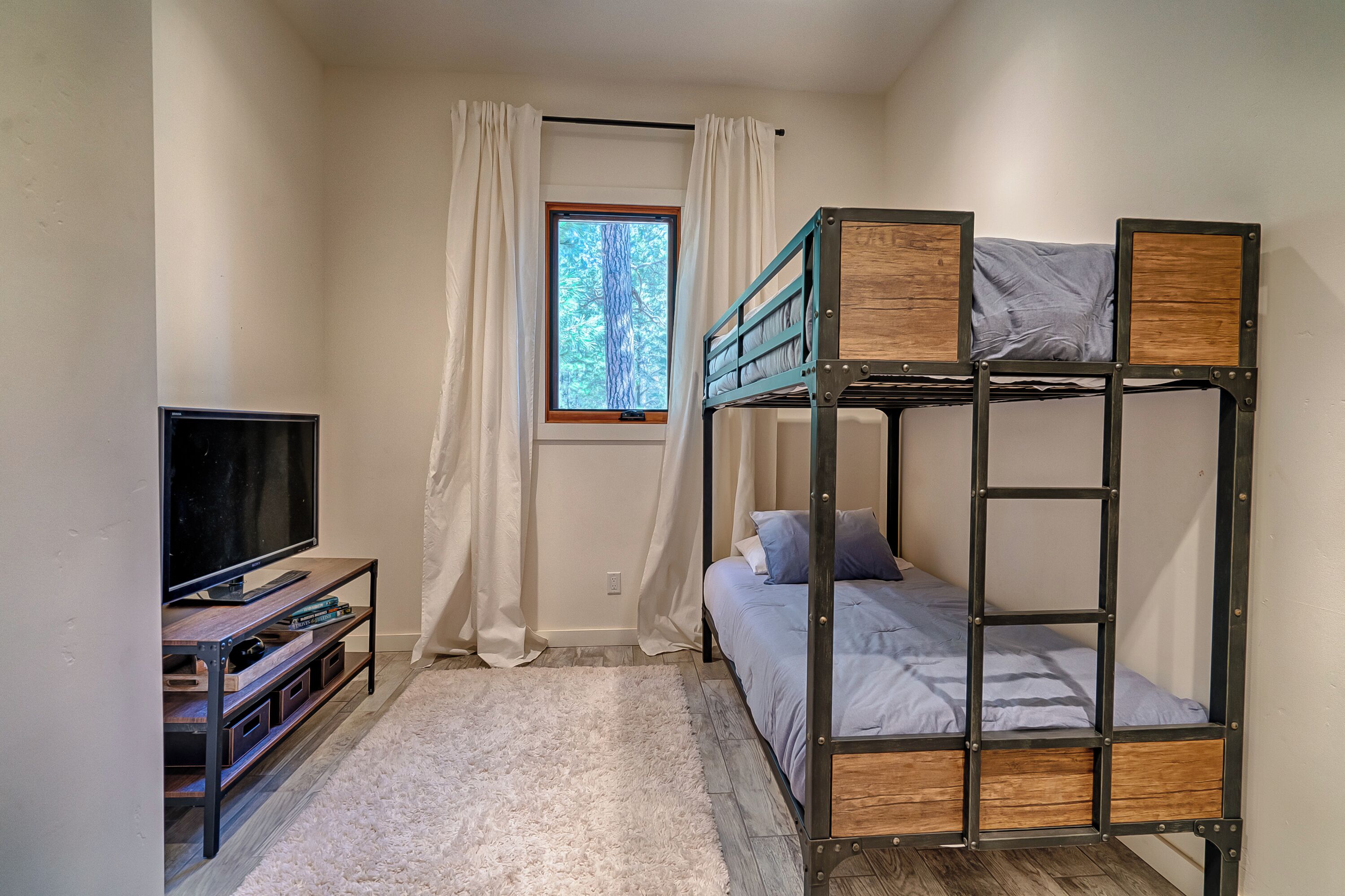 Une chambre avec un lit superposé, un meuble pour la télévision et une fenêtre avec des rideaux.