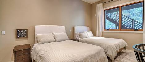 A bedroom with two beds, a nightstand, a window with a view of a staircase, and a motivational quote on the wall.