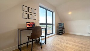 A spacious room with a large window, a desk with a computer and a chair, and a bookshelf. - Stylish & Spacious Apartment (Tunbridge Wells)